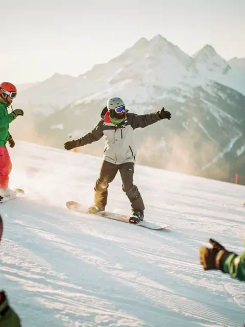 Snowboard instructeur demonstreert techniek aan leerlingen op besneeuwde piste met bergachtergrond in gouden zonlicht