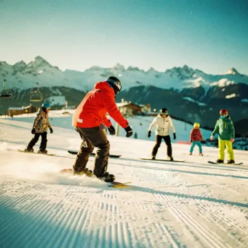 Snowboard instructeur in rode jas demonstreert techniek aan groep studenten op besneeuwde bergpiste bij zonsondergang