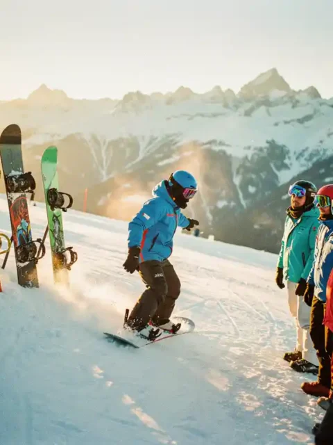 Snowboard instructeur demonstreert techniek aan groep studenten op besneeuwde piste met bergen op achtergrond