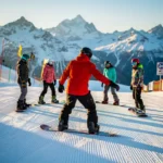 Snowboard instructeur in rode jas toont juiste houding aan groep studenten op besneeuwde piste met bergen op achtergrond