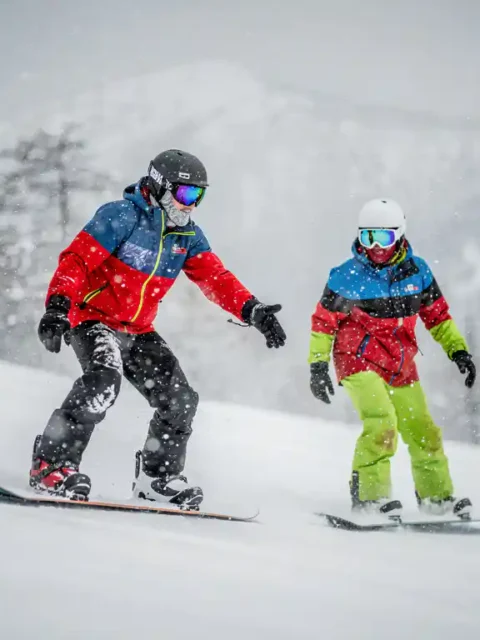 Snowboard instructeur toont techniek aan leerling op besneeuwde berghelling tijdens zware sneeuwval