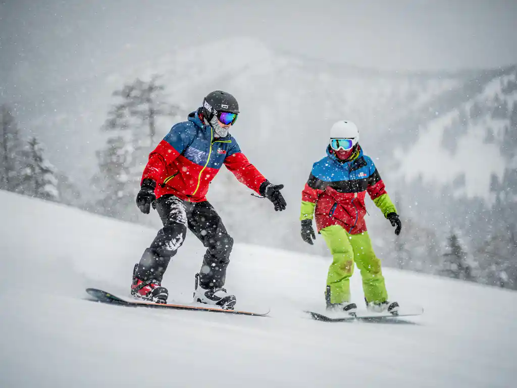 Snowboard instructeur toont techniek aan leerling op besneeuwde berghelling tijdens zware sneeuwval