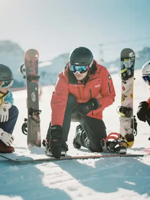 Snowboard instructeur demonstreert techniek aan drie studenten op besneeuwde helling met bergachtergrond