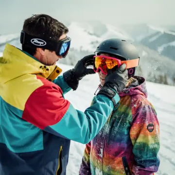 Snowboard instructeur past oranje skibril aan op student's helm tijdens les op besneeuwde bergpiste
