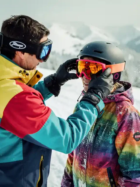 Snowboard instructeur past oranje skibril aan op student's helm tijdens les op besneeuwde bergpiste