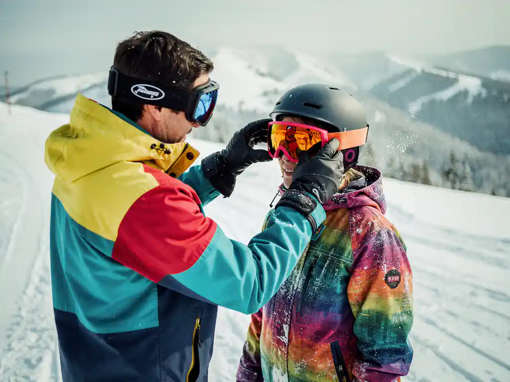 Snowboard instructeur past oranje skibril aan op student's helm tijdens les op besneeuwde bergpiste