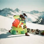Snowboard-Instruktor demonstriert Sturztechnik auf Bergpiste, trägt Helm und Sicherheitsausrüstung, Alpen im Hintergrund