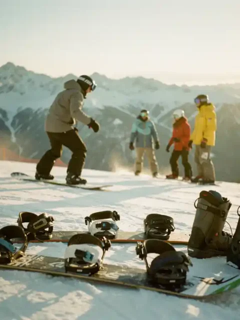 Snowboard-Lehrer zeigt Technik einer Schülergruppe auf verschneiter Bergpiste bei goldenem Sonnenlicht