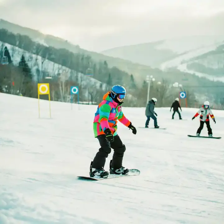 Snowboard-Lehrer zeigt korrekte Haltung auf Anfängerpiste mit grünen und blauen Markierungen im Hintergrund