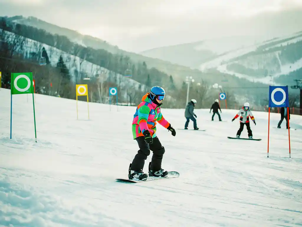 Snowboard-Lehrer zeigt korrekte Haltung auf Anfängerpiste mit grünen und blauen Markierungen im Hintergrund