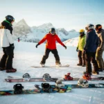 Snowboard-Lehrer in roter Jacke zeigt Anfängern die richtige Haltung auf verschneiter Piste in den Alpen