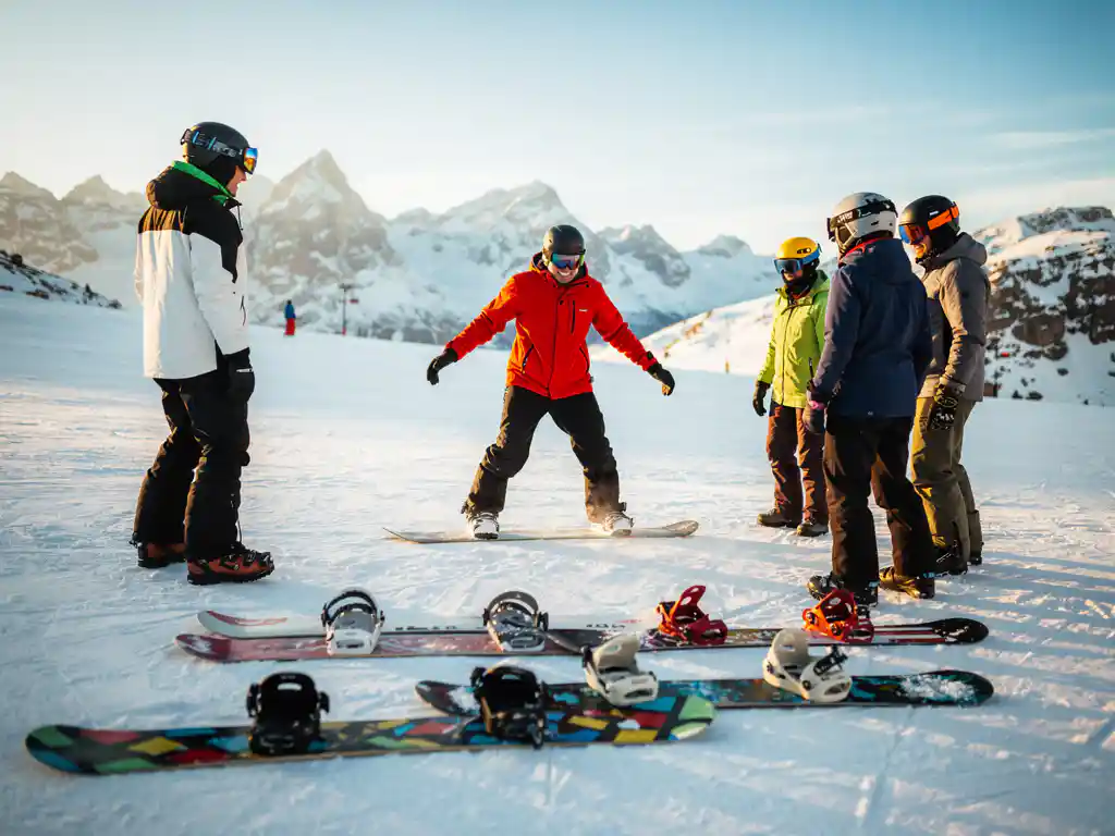 Snowboard-Lehrer in roter Jacke zeigt Anfängern die richtige Haltung auf verschneiter Piste in den Alpen