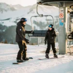 Snowboard-Instruktor zeigt nervösem Anfänger das Einsteigen in den Sessellift vor verschneiten Berghängen