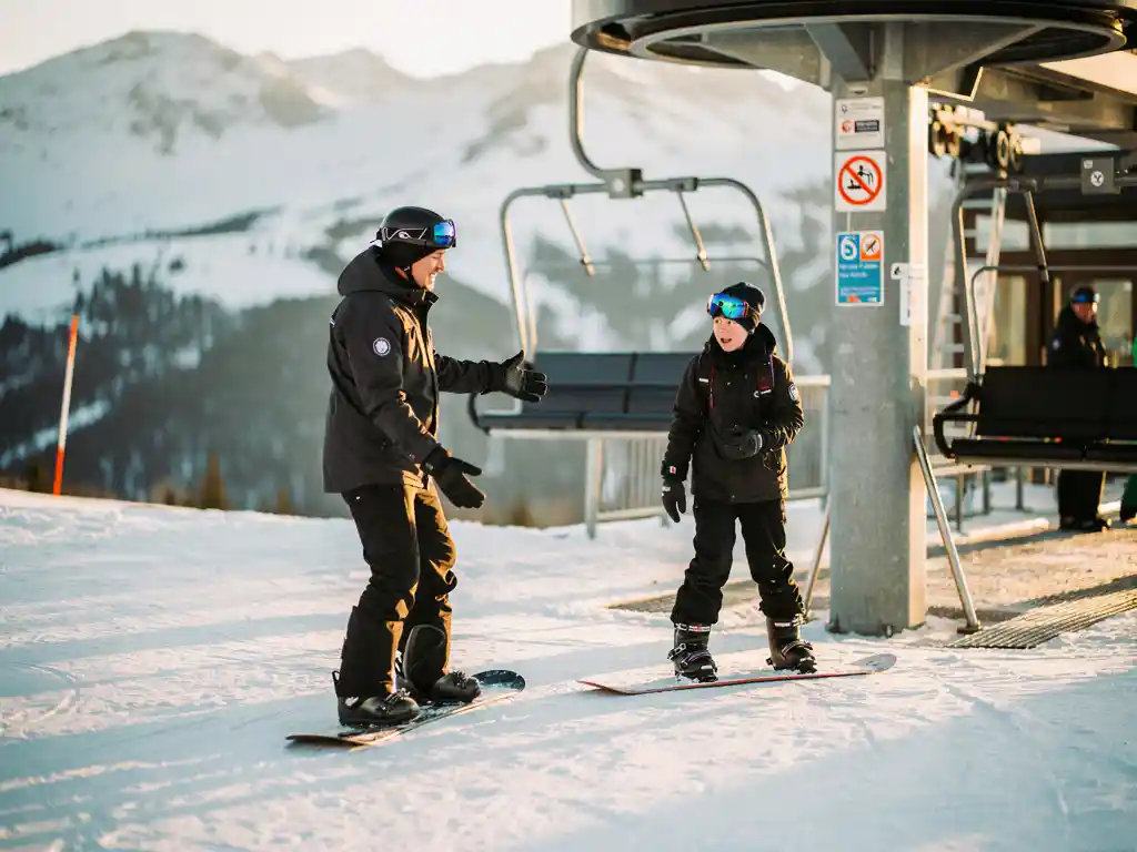 Snowboard-Instruktor zeigt nervösem Anfänger das Einsteigen in den Sessellift vor verschneiten Berghängen