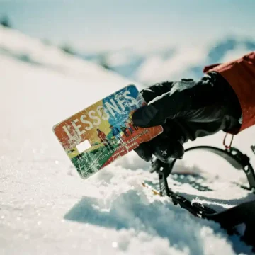 Snowboarder houdt versleten leskaart vast naast snowboardbinding in verse poedersneeuw op zonnige berghelling