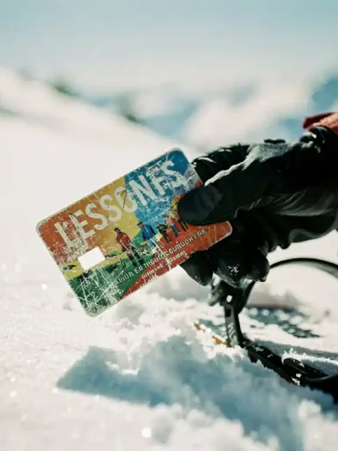 Snowboarder houdt versleten leskaart vast naast snowboardbinding in verse poedersneeuw op zonnige berghelling