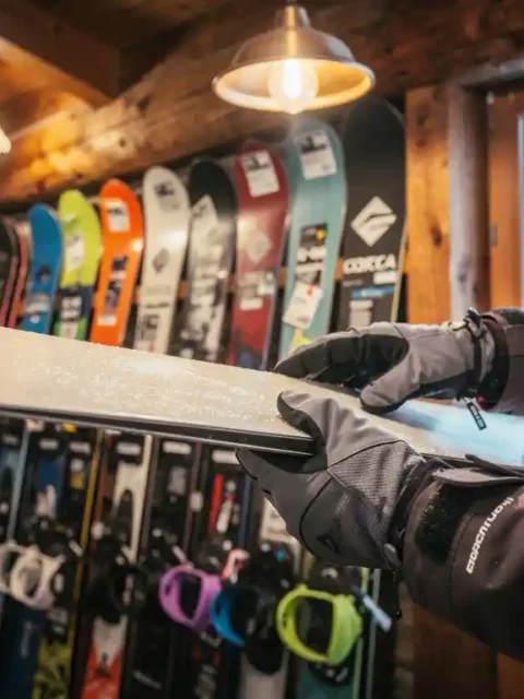 Snowboardeur examinant une planche dans un magasin de location alpin avec équipements colorés sur étagères en bois