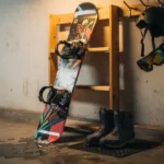 Snowboard tegen houten rek in garage met laarzen, helm en bindingen waar sneeuw vanaf smelt