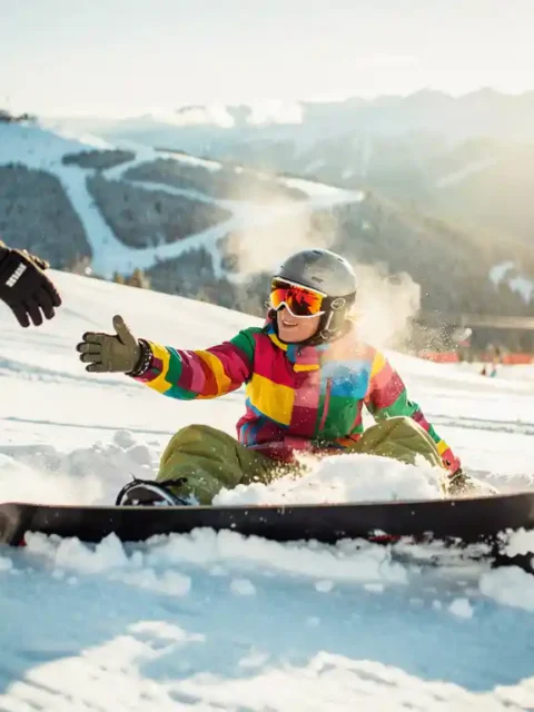 Snowboarder in bunter Winterkleidung nimmt Hilfe vom Skilehrer an, nachdem er im Pulverschnee gestürzt ist