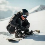 Snowboarder überprüft Bindungen auf frischem Pulverschnee am sonnigen Berghang