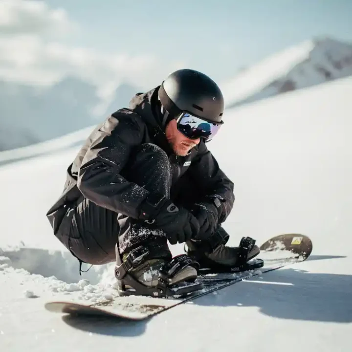 Snowboarder überprüft Bindungen auf frischem Pulverschnee am sonnigen Berghang