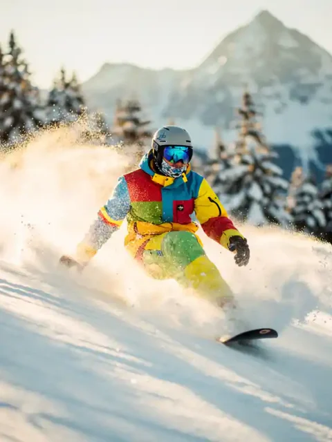 Snowboarder maakt perfecte bocht in poedersneeuw met besneeuwde bergen en dennenbomen op de achtergrond