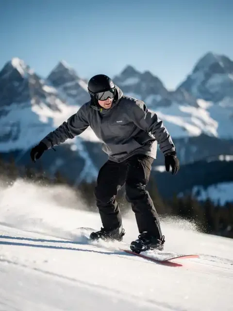 Snowboarder in perfecte rijhouding op verse poedersneeuw met besneeuwde bergtoppen op de achtergrond
