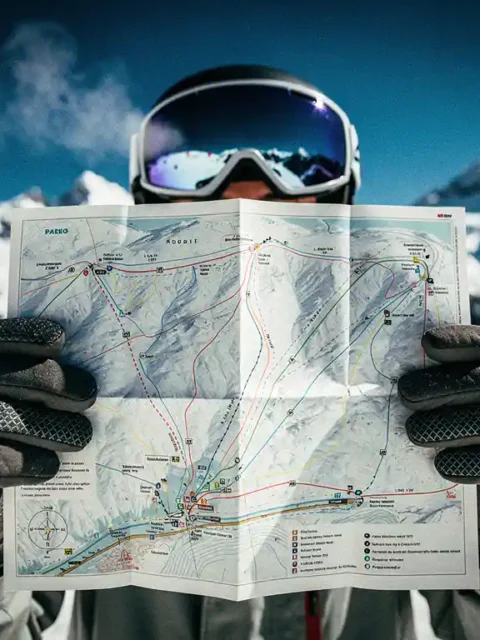Snowboarder houdt pisteplattegrond vast met skihandschoenen tegen besneeuwde bergachtergrond, routekaart duidelijk zichtbaar