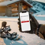 Snowboarder houdt smartphone met annuleringsformulier vast op besneeuwde piste bij berghut tijdens gouden uur