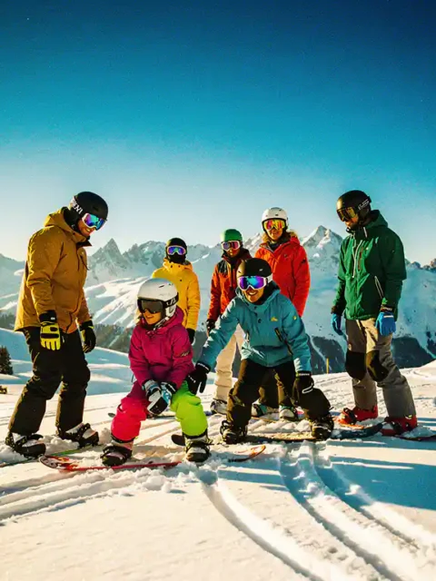 Diverse groep snowboarders van verschillende leeftijden op besneeuwde bergpiste met kleurrijke winterkleding en helmen